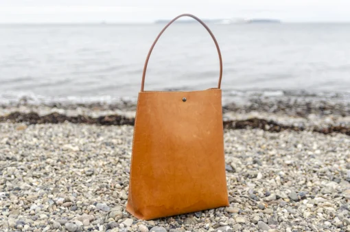 Skuldertaske i læder fra Ida Brink Leather: Anne i natur med patina og klassisk hank - på stranden ved Helgenæs